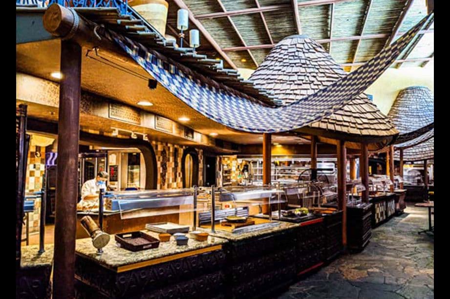Rustic themed buffet restaurant interior with wooden beams, thatched roof details, and food service stations with warm lighting