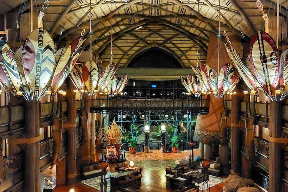 Grand lodge interior with Native American-inspired decor, wooden beams, ceremonial shields, and rustic furniture in multi-level space.
