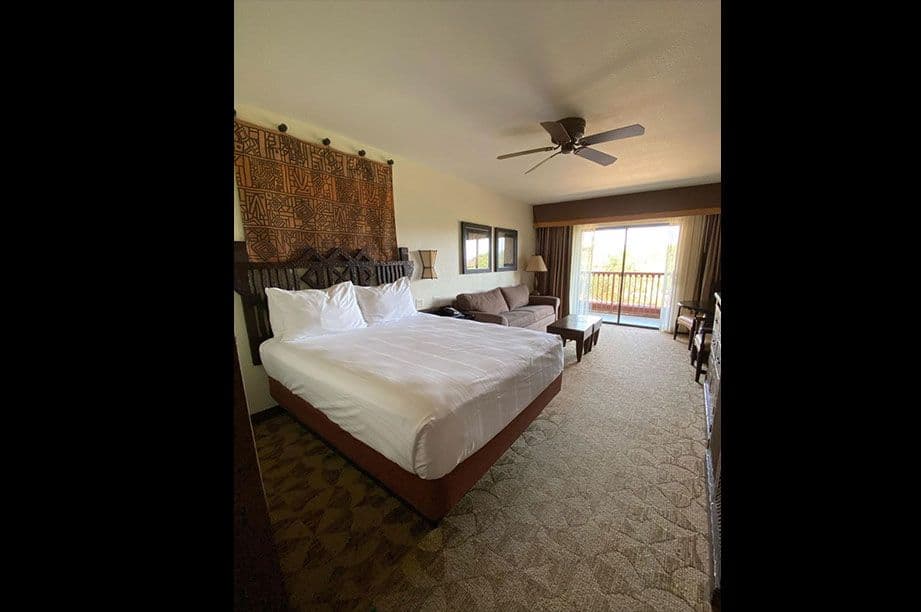 DVC resort bedroom with king bed, decorative headboard tapestry, ceiling fan, balcony doors, and patterned carpet flooring.