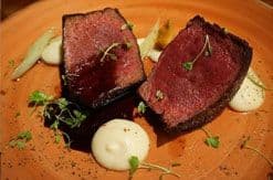 Sliced seared tuna steaks with herbs and sauce on an orange plate, elegantly plated fine dining presentation.