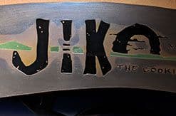 Jiko restaurant sign with metallic lettering reading "Jiko THE COOKING PLACE" on curved wooden surface