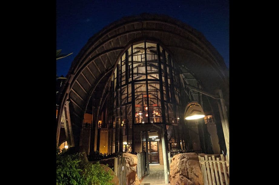 Illuminated curved stone archway entrance to resort building at night with warm interior lighting and landscaping