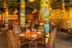 Warm, rustic restaurant dining room with wooden tables, woven chairs, colorful Native American-inspired decor and hanging lanterns.