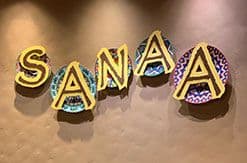 Golden "SANAA" restaurant sign with ornate lettering against a warm, blurred background at Disney's Animal Kingdom Lodge