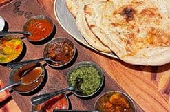 Indian flatbread and colorful curry dishes with various sauces in small bowls arranged on a wooden table