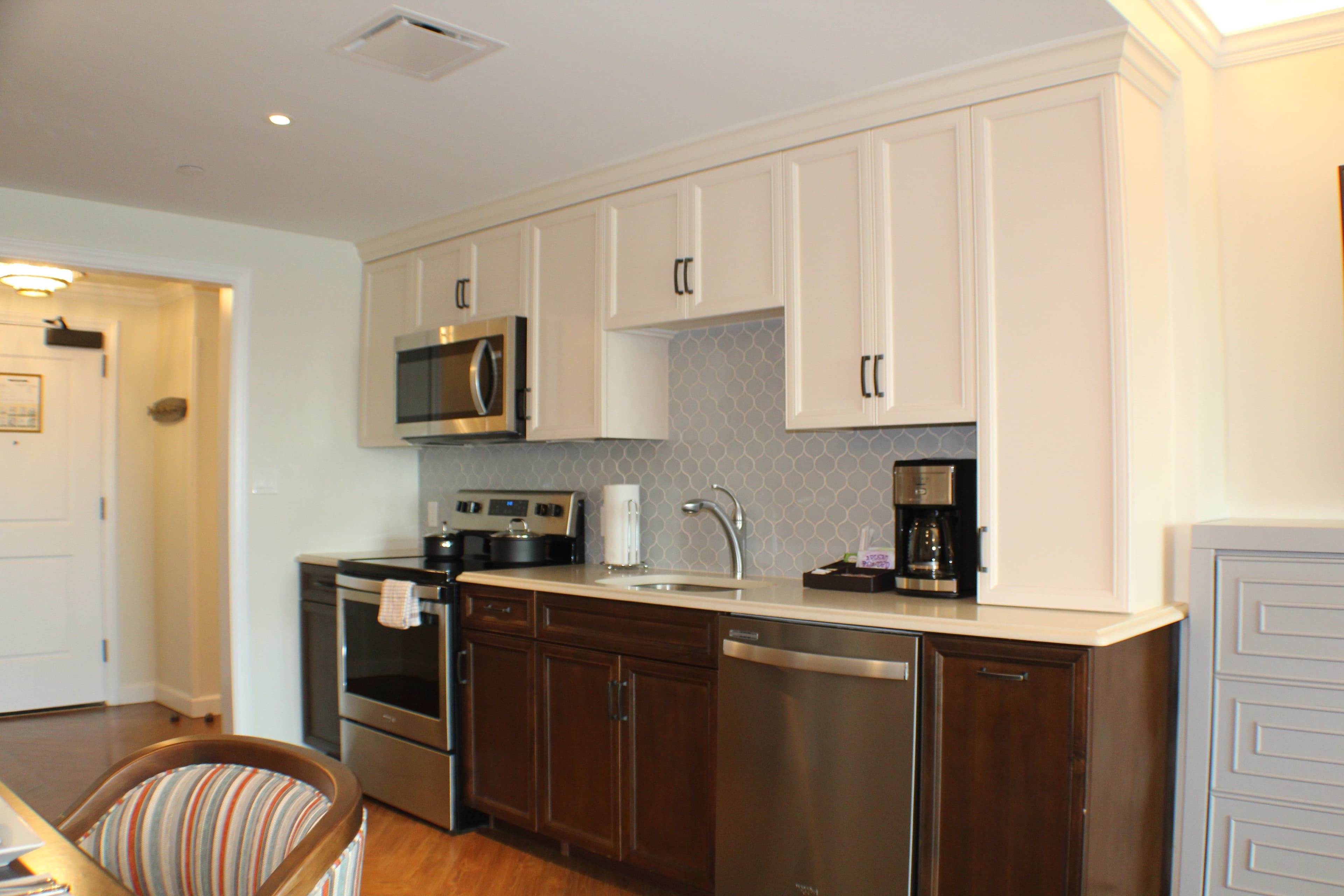 Modern kitchen with white upper cabinets, dark wood lower cabinets, stainless steel appliances, and geometric tile backsplash in vacation rental.