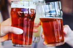 Two glasses of amber-colored beer being held up in a toast at what appears to be a restaurant or bar setting.