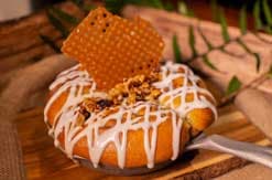 Orange-glazed donut with white icing drizzle and honeycomb garnish on wooden cutting board