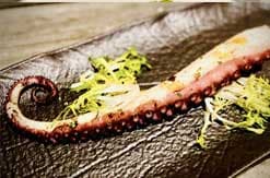 Sliced chocolate tart with berry filling and yellow garnish on rustic wooden surface with burlap textile