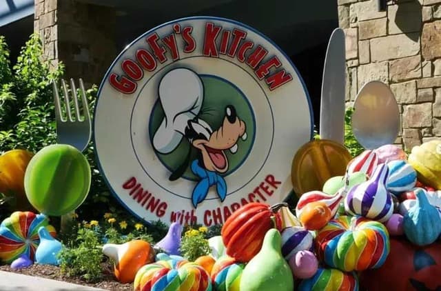 A sign for goofy's kitchen with a bunch of balloons in front of it