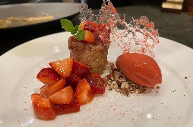 Elegant plated dessert with strawberry cake, fresh berries, sorbet, chocolate crumbs and decorative sugar work on white plate