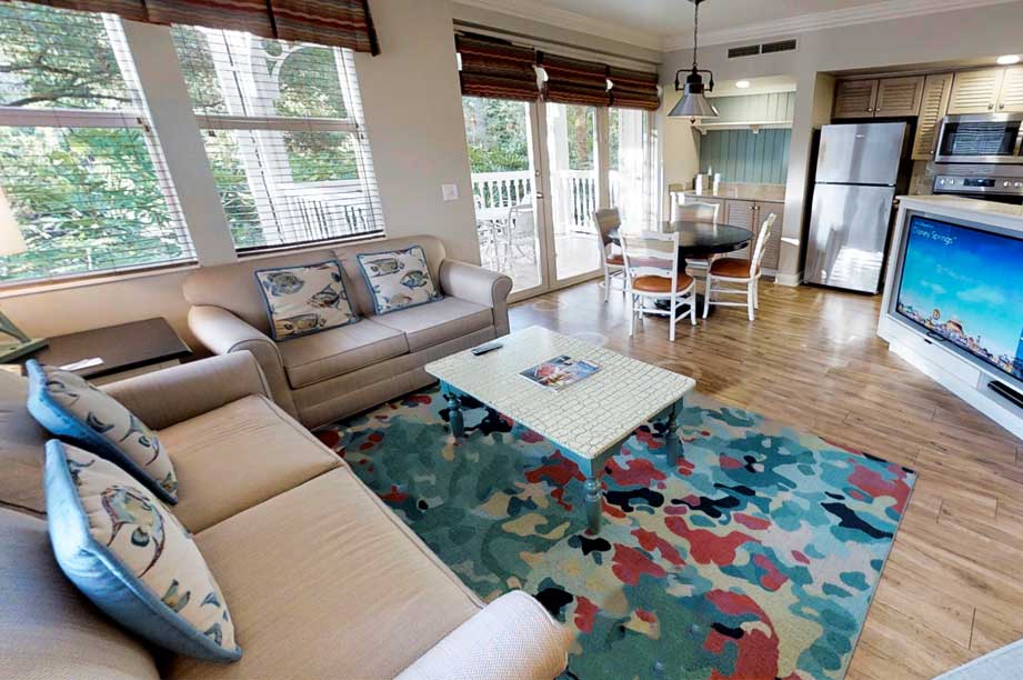 Modern resort living room with gray sectional sofa, colorful area rug, hardwood floors, and open kitchen with stainless appliances.