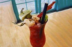 Tropical red cocktail garnished with fruit and decorative umbrella on wooden table near window overlooking water