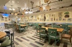 Modern restaurant dining room with green booth seating, striped flooring, exposed ceiling, and wall-mounted artwork throughout.