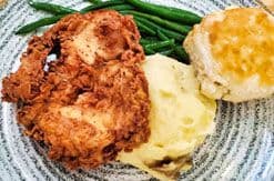 Fried chicken with mashed potatoes, gravy, green beans, and a biscuit served on a white plate