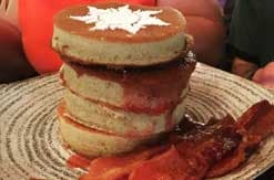 Stack of festive holiday cookies with white icing and red filling on woven placemat with decorative red napkin