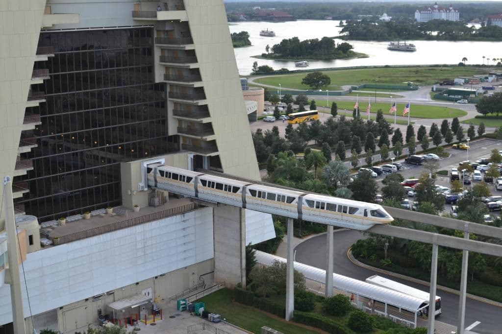 Monorail train traveling on elevated track past modern resort hotel with lake and green spaces visible in background