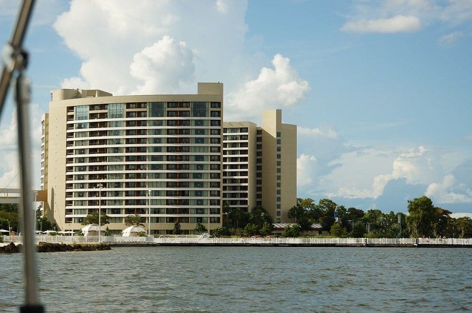 Large beige waterfront resort hotel with multiple floors and balconies viewed from across a body of water on a sunny day.