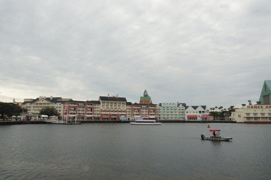 Waterfront view of Disney's BoardWalk Resort with colorful buildings, boat on lake, and overcast sky