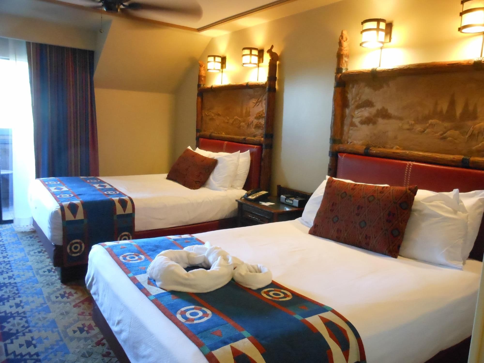 Hotel room with two beds featuring colorful Southwest-themed bedding, decorative headboards with lantern lighting, and towel animals.