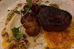 Grilled steak with herb garnish and roasted potatoes on white plate, seasoned with black pepper and herbs