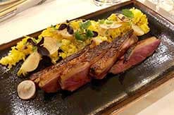 Sliced steak served on a dark wooden board with yellow flowers and mushroom garnish at a Disney resort restaurant.