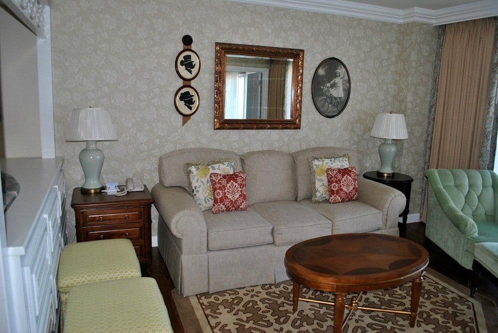 Elegant living room with beige sofa, red accent pillows, dark wood coffee table, mint green tufted chair, and traditional decor.