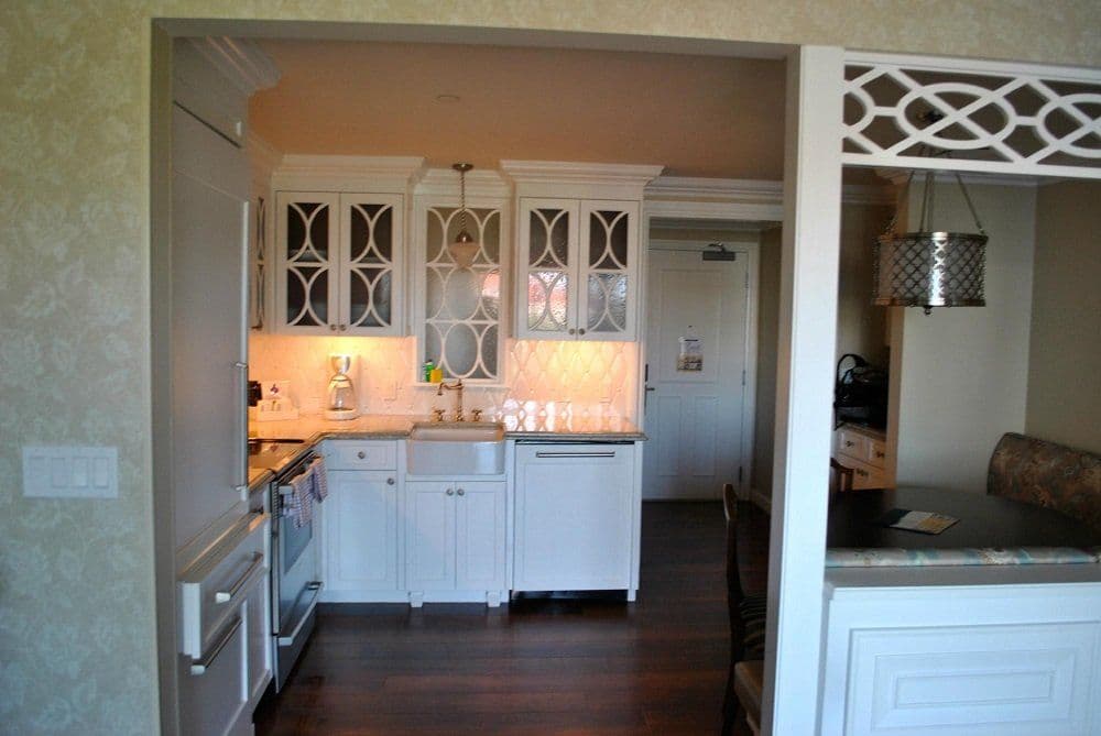 Kitchen with white cabinets, glass doors, marble backsplash, dark hardwood floors, and decorative white trim opening to dining area